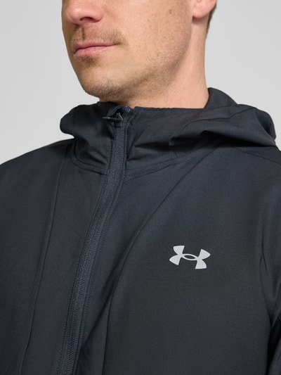 Männermodel trägt Regular Fit Jacke mit Logo-Print Modell 'Unstoppable' von Under Armour, dunkler Stoff, Reißverschluss, Nahaufnahme Oberkörper. Elastischer Material-Mix, Kapuze mit Stehkragen, sportlicher Look.