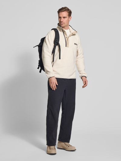 Męski model nosi Fleecepullover mit Stehkragen und Knopfleiste od Columbia, krój regular fit, wyhaftowane logo, kieszeń zapinana na zamek, długość tyłu 73 cm, długość rękawów 70 cm; kolory kremowy i czarny, gładka tekstura; widok całej sylwetki z przodu.