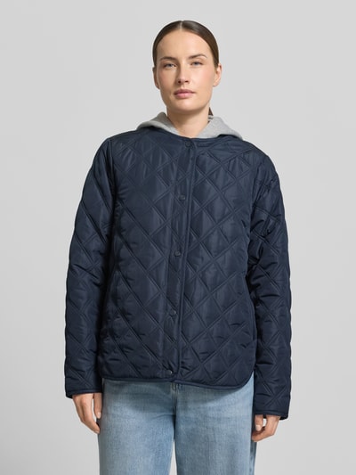 Kobiece model prezentuje Regular Fit Jacke in Stepp-Optik mit Kapuze Modell 'Fenya' von Soyaconcept, kolor granatowy, z efektem pikowania, krój regular fit, kaptur, wpuszczane kieszenie, listwa guzikowa na całej długości, długość tyłu w rozmiarze S: 65 cm, szerokość ramion w rozmiarze S: 40 cm, szerokość w rozmiarze S: 54 cm, długość rękawów w rozmiarze S: 65 cm, widok całej sylwetki z przodu.