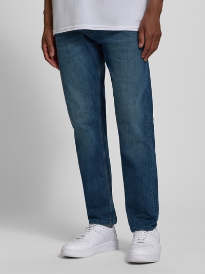 Männermodel trägt Tapered Fit Jeans aus Baumwoll-Mix von s.Oliver RED LABEL in mittlerem Blau, glatte Textur, Ganzkörperansicht von vorne.