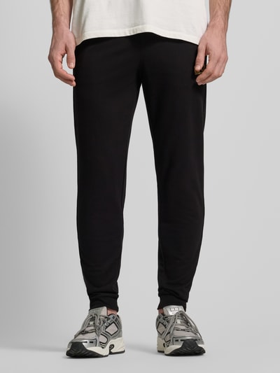 Männermodel trägt Sweatpants mit Logo und elastischem Bund von EA7 Emporio Armani, schwarze Farbe, Baumwoll-Elasthan-Mix, Ganzkörperansicht von vorne.