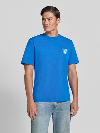 Männermodel trägt Regular Fit T-Shirt aus reiner Baumwolle Modell 'VIBING COCO' von REVIEW in Blau, Print seitlich, Ganzkörperansicht von vorne, Herren T-Shirt von REVIEW x ANSON´S, Rückenlänge bei Größe M 68 cm.