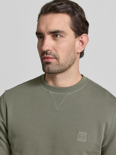 Mężczyzna nosi Relaxed Fit Sweatshirt aus reiner Baumwolle Modell 'WESTART' von BOSS Orange, jednolity zielony kolor, okrągły dekolt, długi rękaw, patch z logo, materiał: czysta bawełna, zbliżenie na górną część ciała