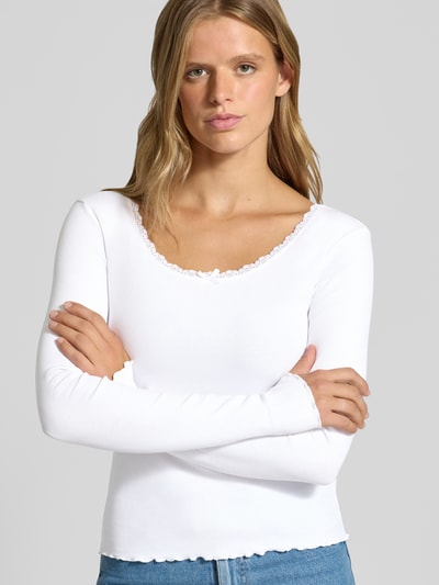 Kobiece modelka ma na sobie Longsleeve mit Spitzenbesatz und Rundhalsausschnitt od REVIEW, mieszanka bawełny i elastanu, krój slim fit, efekt prążkowania, obszycie koronką, okrągły dekolt, długość tyłu w rozmiarze S: 50 cm, zbliżenie na górną część ciała z przodu.