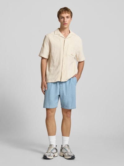 Męski model nosi Regular Fit Freizeithemd mit Logo-Stitching von REVIEW z bawełny, kremowy, faktura prążkowana, przód, krój regular fit, kołnierz rewersowy, kieszeń na piersi, logo, długość tyłu 68 cm, szerokość w rozmiarze M 55 cm, długość rękawa 27 cm, ujęcie całej sylwetki z przodu.