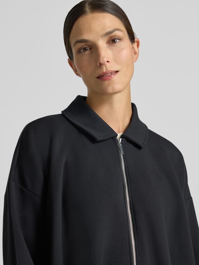 Frauenmodel trägt Sweatjacke mit Umlegekragen von Christian Berg Woman in Schwarz, glatte Textur, lockere Passform, Nahaufnahme Oberkörper, Modal-Mix, überschnittene Schultern, Reißverschluss, elastische Abschlüsse.