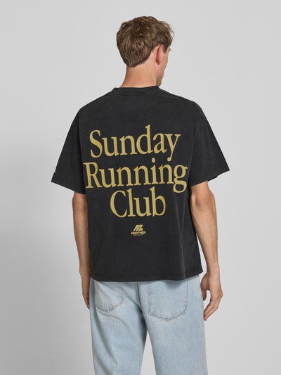 Mężczyznamodel nosi T-Shirt mit Print und Rundhalsausschnitt von ANOTHER COTTON LAB z bawełny, krój relaxed fit, nadruk, okrągły dekolt, długość tyłu w rozmiarze M: 69 cm, czarny z żółtym nadrukiem, proste krawędzie, gładka tekstura. Ganzkörperansicht Rückansicht.