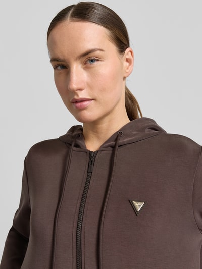 Frauenmodel trägt Sweatjacke mit Kapuze Modell 'OLYMPE' von Guess Activewear im Material-Mix mit Modal-Anteil, Regular-Fit, Label-Applikation, Reißverschluss, braune Farbe, glatte Textur, Nahaufnahme Oberkörper.