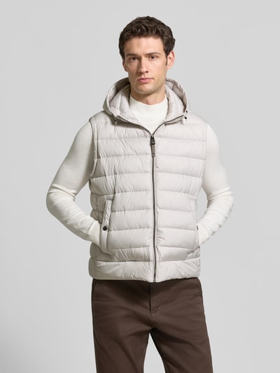 Männermodel trägt hellgraue, wattierte Steppweste mit Kapuze von JOOP!, kombiniert mit weißem Pullover, Ganzkörperansicht von vorne.