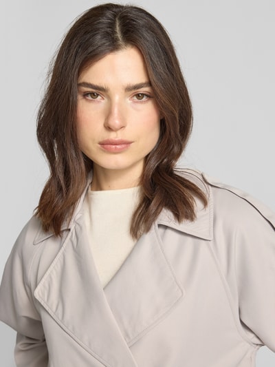 Kobiece model prezentuje Regular Fit Trenchcoat mit Schulterriegeln von Tom Tailor Denim, efekt: jednolity kolor, krój regular fit, kołnierz z połami, listwa guzikowa, patki przy mankietach, wpuszczane kieszenie, wykończenie materiału: splot twill, zbliżenie na górną część ciała.