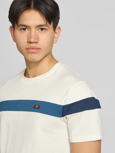 Männermodel trägt Regular Fit T-Shirt mit Logo-Detail Modell 'Caserio' von Ellesse, cremefarben mit blauem Streifen, Nahaufnahme Oberkörper. Baumwolle, Rundhalsausschnitt, kurzärmelig, Rückenlänge ca. 68 cm bei Größe M.