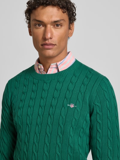 Mężczyznę model nosi Sweter z dzianiny z ściegiem warkoczowym i wyhaftowanym logo od Gant, bawełna, krój slim fit, okrągły dekolt, Nahaufnahme Oberkörper.
