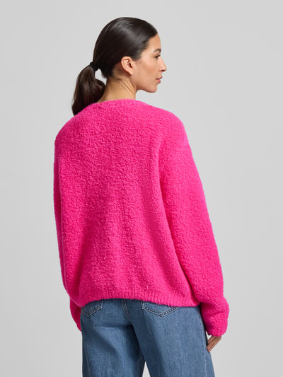 Frauenmodel trägt Strickjacke mit Knopfleiste Modell 'ZOLLY' von American Vintage in Pink, lockerer Schnitt, Lanawoll-Mix mit Alpaka, Gerippte Abschlüsse, Rückenansicht Ganzkörperansicht.