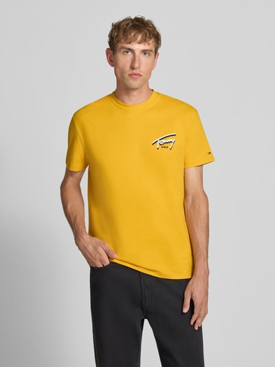 Männermodel trägt Regular Fit T-Shirt aus reiner Baumwolle von Tommy Jeans in Gelb mit kleinem Logo, Ganzkörperansicht von vorne.