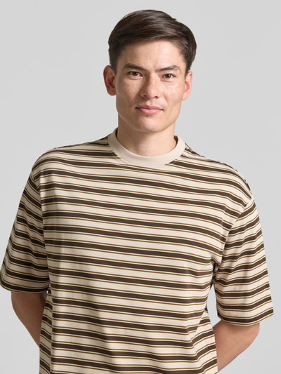 Mężczyznmodel nosi męski t-shirt Relaxed Fit T-Shirt aus reiner Baumwolle Modell 'ASPEN 2' von SELECTED HOMME, beżowe i brązowe paski, tekstura gładka, Nahaufnahme Oberkörper.