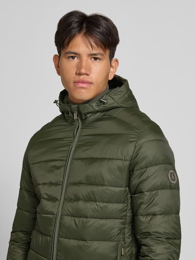 Męski model nosi Regular Fit kurtka z efektem pikowania Model 'KINGSLEY' od JACK & JONES w kolorze oliwkowym, kaptur, zamek błyskawiczny, wpuszczane kieszenie, Szerokość tyłu w rozmiarze M: 70 cm, Szerokość ramion w rozmiarze M: 45 cm, Szerokość klatki piersiowej w rozmiarze M: 52 cm, Długość rękawów w rozmiarze M: 67 cm, zbliżenie na górną część ciała.