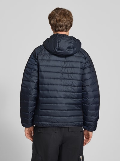 Männermodel trägt dunkelblaue Regular Fit Steppjacke mit Reißverschluss von adidas Originals, glatte Textur, Ganzkörperansicht Rückansicht.