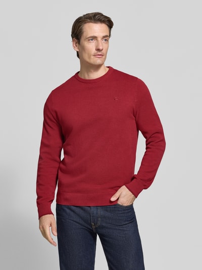 Männermodel trägt Regular Fit Strickpullover aus reiner Baumwolle mit Label-Detail von LERROS, rote Farbe, elastische Abschlüsse, Ganzkörperansicht von vorne. Rückenlänge 68 cm, Ärmellänge 69 cm, glatte Textur.