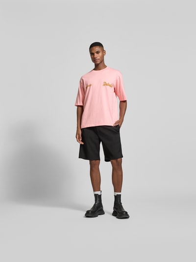 Männermodel trägt Loose Fit T-Shirt mit Logo-Stitching von Dsquared2 in Rosa aus Baumwolle, schwarze Shorts, Ganzkörperansicht von vorne.