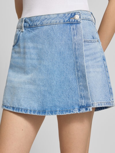 Frauenmodel trägt Jeans-Skort in hellblauer Waschung von REVIEW, Reine Baumwolle, Wickel-Optik, Eingrifftasche, Gesäßtaschen, Nahaufnahme Oberkörper.