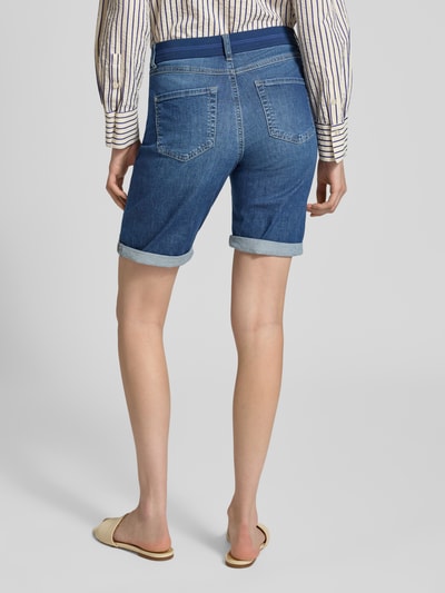 Männermodel trägt Jeansshorts mit Umschlag und elastycznym pasem von Angels, bawełna z domieszką elastanu, krój regular fit, szerokość w rozmiarze 36: 39 cm, długość wewnętrzna nogawki w rozmiarze 36: 30 cm, odcień niebieskiego, tekstura jeansu, widok całej sylwetki z tyłu