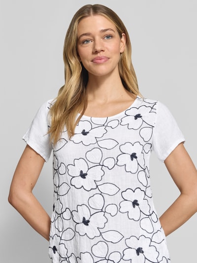 Frauenmodel trägt Minikleid aus Leinen-Mix im Allover-Look Modell 'No44vaa' von ZABAIONE mit floralen Stitchings, Nahaufnahme Oberkörper. Leichter Stoff in Weiß mit dunkel abgesetztem Blumenmuster, gerader Schnitt, Rundhalsausschnitt, Kontext: Damen Minikleid mit Baumwoll-Anteil.