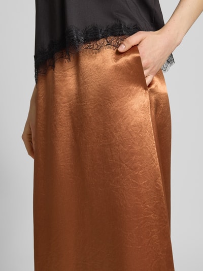 Kobiece modelka nosi długą spódnicę z satyny o linii a, model 'TUONO' od MM by Max Mara, elastyczny pas, kolor miedziany, detal przy kieszeni, całkowita długość 106 cm w rozmiarze 36, szerokość w rozmiarze 36: 37 cm, zbliżenie na biodra.