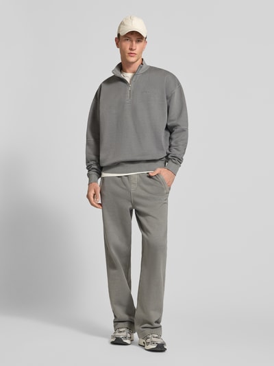 Männermodel trägt Relaxed Fit Sweatshirt aus Mieszanka bawełny von PEGADOR w kolorze szarym z wyhaftowanym logo, ozdobne szwy, prążkowane wykończenia, kołnierz zapinany, długi rękaw, długość tyłu 72 cm, długość rękawów 65 cm, Ganzkörperansicht von vorne.