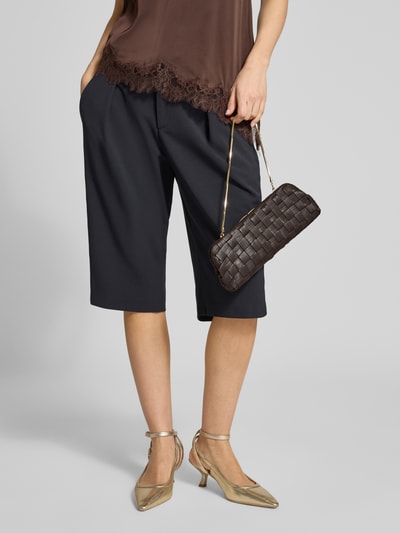 Frauenmodel trägt Clutch mit echtem Kupfer Modell 'Selva' von Mango mit Strukturmuster, Abnehmbarer Schulterriemen, Hauptfach mit Schnappverschluss, Produktgröße 28 cm Breite, 12 cm Länge, 3 cm Tiefe, Schulterriemen 49 cm, Ganzkörperansicht von vorne.