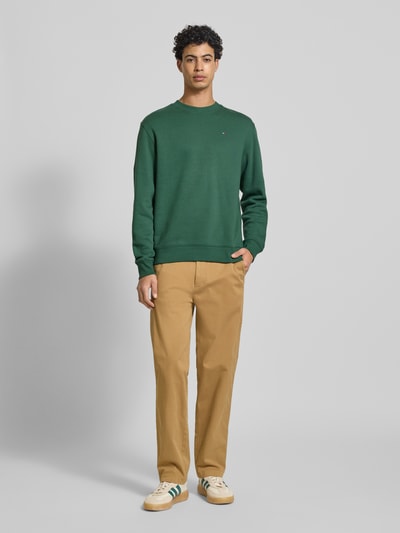 Männermodel trägt Tapered Chino aus Baumwoll-Mix Modell 'SONNY' von Tommy Jeans, efekt: jednolity kolor, krój regular fit, szlufki na pasek, zapięcie na guzik i kryty zamek błyskawiczny, wpuszczane kieszenie, kieszenie z tyłu, kieszonka na monety, splot twill, mieszanka bawełny, całkowity widok z przodu.