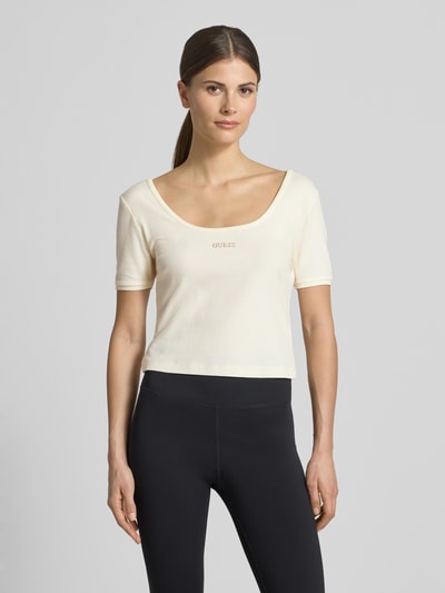 Frauenmodel trägt Cropped T-Shirt aus Lyocell-Mix Modell 'Circe' von Guess Activewear in Creme mit Logo-Stitching, feine Rippstruktur, Ganzkörperansicht von vorne.