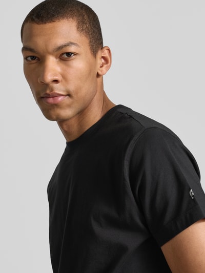 Męski model ma na sobie Regular Fit T-Shirt mit Logo-Print od Fabletics, czarny, bawełniany materiał, krój regular fit, logo z nadrukiem, okrągły dekolt, długość tyłu w rozmiarze M: 65 cm, zbliżenie na górną część ciała.