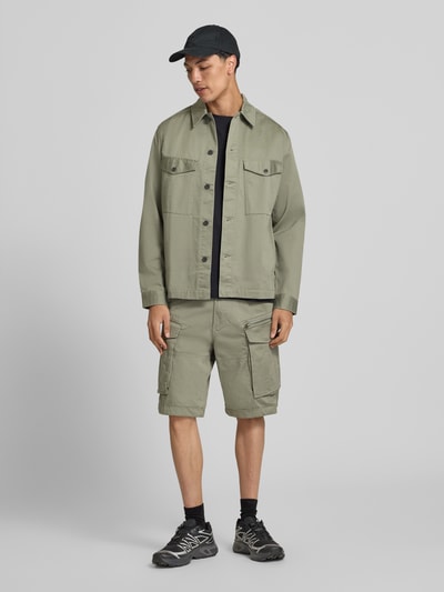 Męski model nosi bermudy z patkami model 'ROVIC ZIP' od G-Star Raw, mieszanka bawełny z dodatkiem streczu, krój straight fit, zapięcie na guzik i zamek błyskawiczny, 5 kieszeni, kieszenie z patkami i zamkiem błyskawicznym, z tyłu kieszeń z wypustką, szerokość w rozmiarze 32: 44 cm, długość wewnętrzna nogawki w rozmiarze 32: 28 cm, jasna zieleń, prosty fason, gładka tekstura. Ganzkörperansicht von vorne.