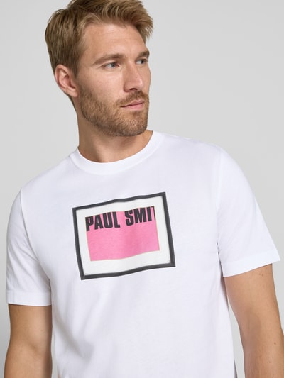 Männermodel trägt T-Shirt mit Label-Print von Paul Smith in Weiß mit rosa und schwarzem Print, reine Baumwolle, Regular Fit, Rundhalsausschnitt, Nahaufnahme Oberkörper.