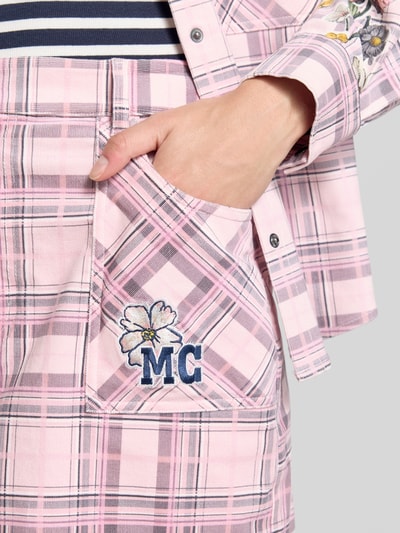 Frauenmodel trägt Minirock aus Baumwoll-Mix von Marc Cain in Rosa mit Karomuster, Logo-Stitching, aufgesetzte Eingrifftaschen, Nahaufnahme Oberkörper.