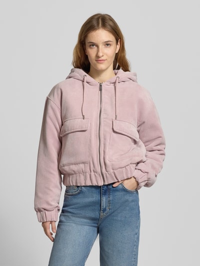 Frauenmodel trägt Regular Fit Bomberjacke mit Kapuze Modell 'SUVA' von Only in Rosa, Cord-Struktur, aufgesetzte Taschen, Ganzkörperansicht von vorne.