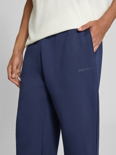 Männermodel trägt Straight Fit Sweatpants Baumwoll-Mix von REVIEW in Dunkelblau mit seitlichen Eingrifftaschen und Label-Print, Nahaufnahme Oberschenkel