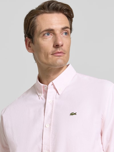 Männermodel trägt Regular Fit Freizeithemd aus reiner Baumwolle von Lacoste in zartem Rosa mit Button-down-Kragen, Nahaufnahme Oberkörper. Herren Freizeithemd von Lacoste