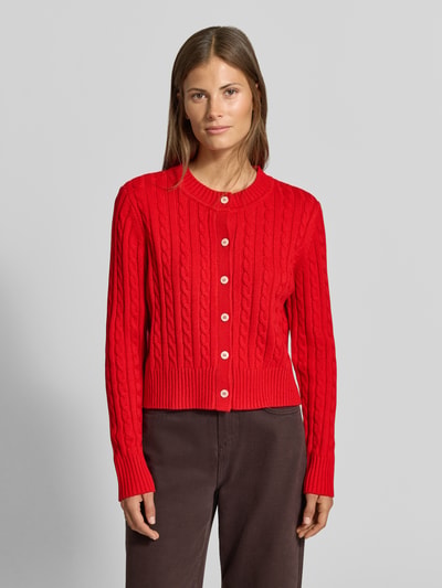 Frauenmodel trägt Strickjacke mit Woll-Anteil von MYON in Rot, Zopfmuster, gerade Passform, gerippte Abschlüsse, Ganzkörperansicht von vorne