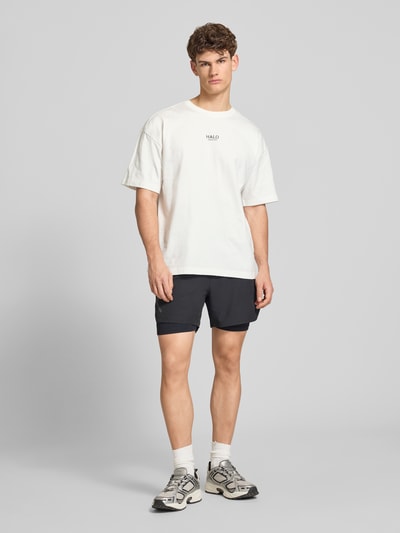 Männermodel trägt Boxy Fit T-Shirt mit Label-Print von ELITE in Weiß, reine Baumwolle, Rundhalsausschnitt, Ganzkörperansicht von vorne.
