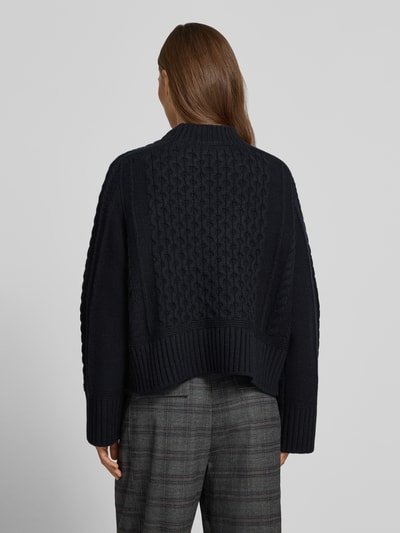 Frauenmodel trägt Strickpullover mit Zopfmuster von Style Icon Collection, dunkle Farbe, lockere Passform, Ganzkörperansicht Rückansicht. Reine Baumwolle, Rundhalsausschnitt, gerippte Abschlüsse, Rückenlänge 46 cm, Ärmellänge 71 cm.