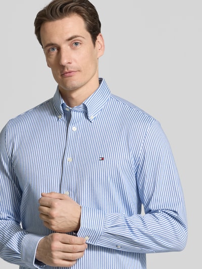 Männermodel trägt Regular Fit Freizeithemd aus Baumwoll-Mix von Tommy Hilfiger, blau-weiß gestreift, Logo-Detail, Nahaufnahme Oberkörper.