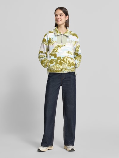 Modelka nosi Fleecepullover mit Stehkragen und Reißverschlusstaschen od Columbia, krój regular fit, stójka, detal z logo, kieszenie zapinane na zamek błyskawiczny, długość tyłu w rozmiarze S 60 cm, szerokość ramion w rozmiarze S 56 cm, szerokość klatki piersiowej w rozmiarze S 55 cm, długość rękawów w rozmiarze S 57 cm, wzór w odcieniach zieleni, bieli i błękitu, miękka tekstura, pełny widok z przodu