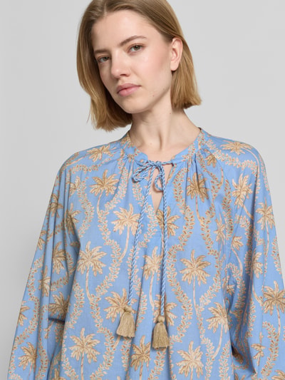 Frauenmodel trägt Bluse mit Tunikakragen und Quasten von Emily Van den Bergh in Blau mit beigem Palmenmuster, reine Baumwolle, Loose Fit, Nahaufnahme Oberkörper.