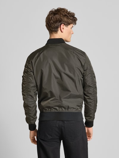 Męski model ma na sobie Regular Fit Bomberjacke mit Logo-Patch od Alpha Industries, ciemnozielony materiał o gładkiej fakturze, widok całej sylwetki z tyłu, długość tyłu 65 cm, szerokość ramion 45 cm, szerokość w rozmiarze M 54 cm, długość rękawa 69 cm