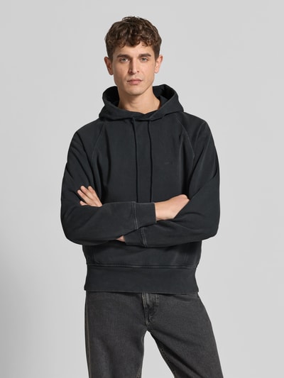 Männermodel trägt Regular Fit Hoodie aus reiner Baumwolle von Closed in Schwarz, sichtbare Känguru-Tasche, Nahaufnahme Oberkörper.