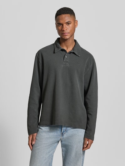 Mężczyzna nosi Loose Fit Poloshirt aus Baumwolle Modell 'Thiago' von Wood Wood, kolor ciemnoszary, długi rękaw, czysty bawełna, haft z logo, widok całej sylwetki z przodu.
