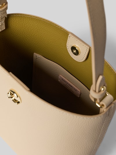 Produktfoto, saszetka Pochette mit Schulterriemen Modell 'NIKLA' von Coccinelle, beżowa struktura, główna przegroda z zapięciem na magnes, aplikacja z metką, Szerokość w rozmiarze 1: 24 cm, długość w rozmiarze 1: 20 cm, głębokość w rozmiarze 1: 10 cm, długość paska na ramię w rozmiarze 1: 116 cm