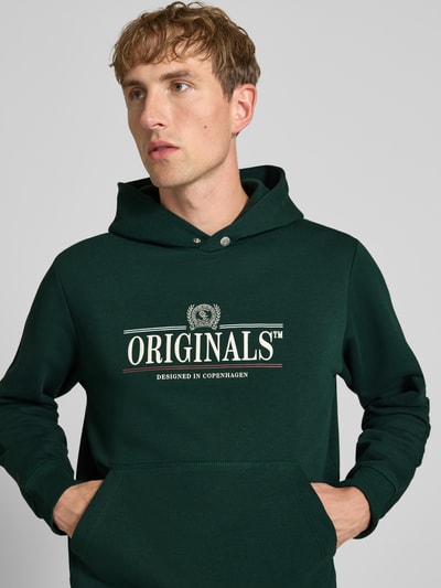 Männermodel trägt Hoodie mit Label-Print Modell 'FREDERIKSBERG' von JACK & JONES in Dunkelgrün, Baumwoll-Mix, Nahaufnahme Oberkörper.