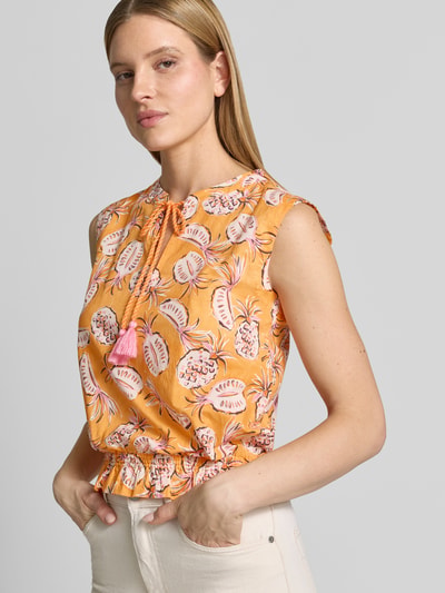 Frauenmodel trägt Regular Fit Bluse im Ärmellosen-Design von Emily Van den Bergh aus Reiner Baumwolle mit Allover-Motiv-Print, Rüschenbesatz am Bund und Schlüsselloch-Ausschnitt, Rückenlänge bei Größe 36: 54 cm, leuchtende Orange- und Rosatöne, glatte Textur. Nahaufnahme Oberkörper.